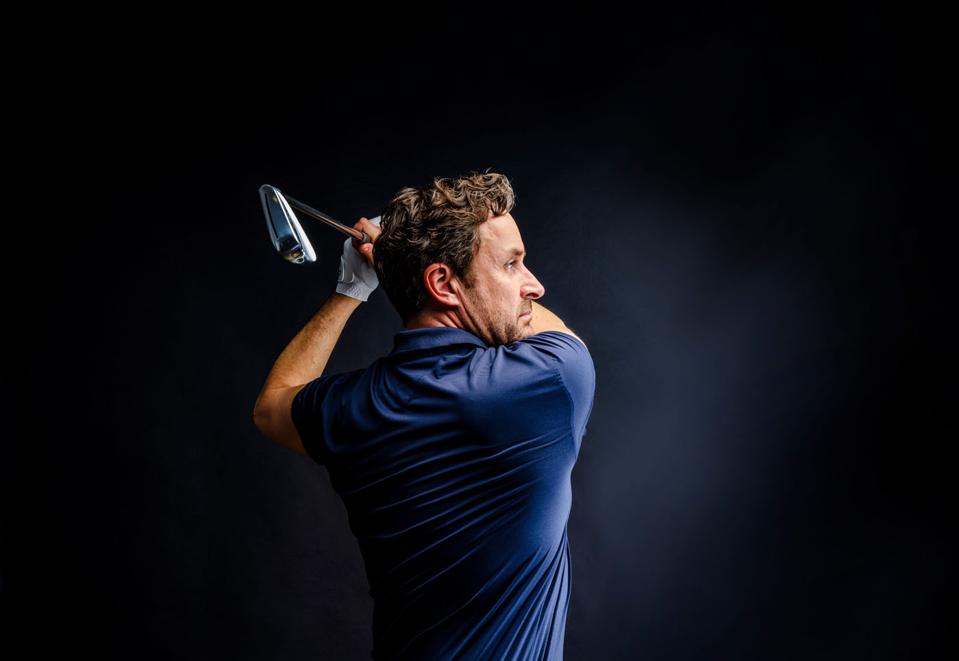 The profile of a man who is swinging his club in a Tee Box golf course.